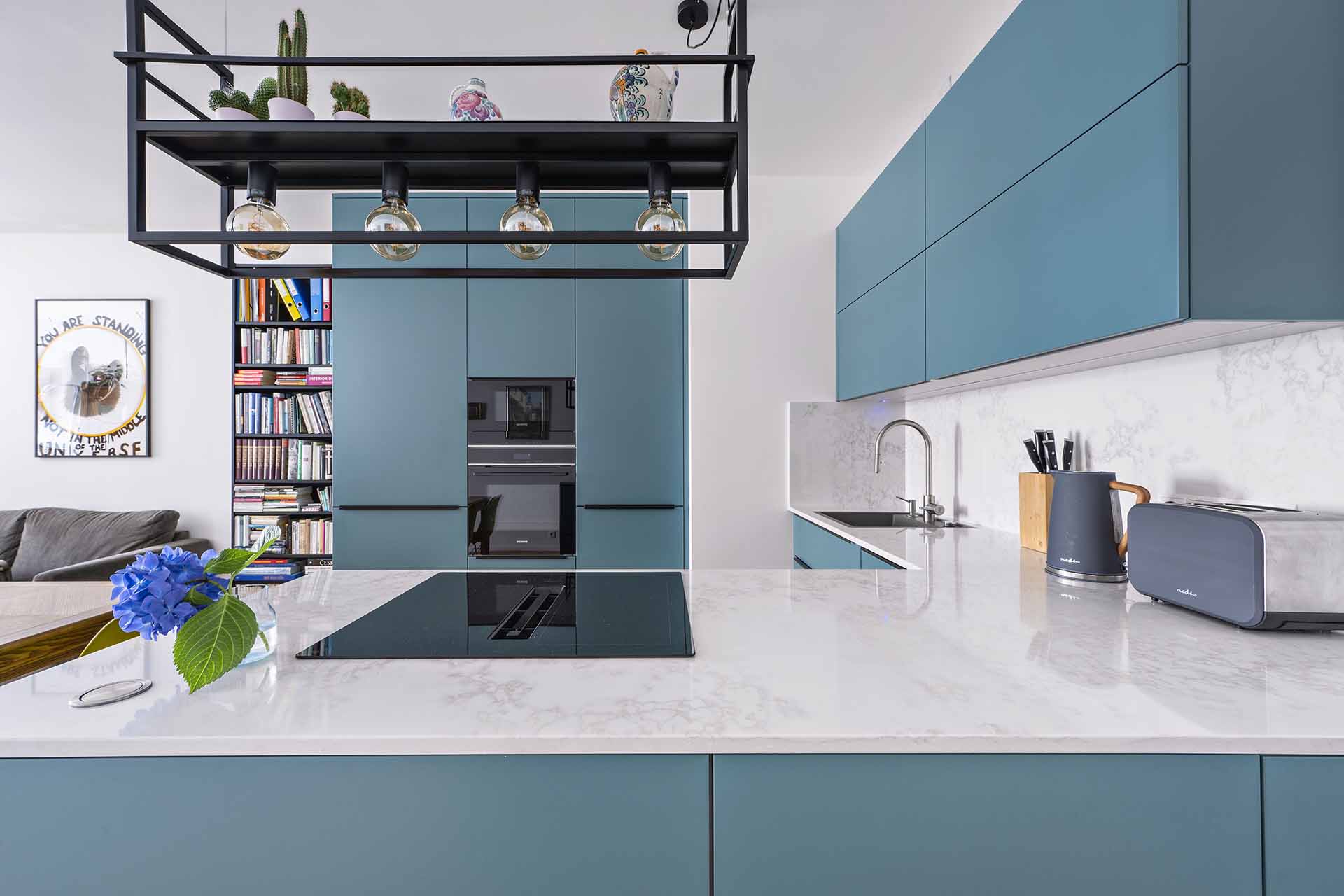 Jídelní kout s masivním dřevěným stolem, žlutými židlemi a kuchyní na míru v petrolejovém odstínu.