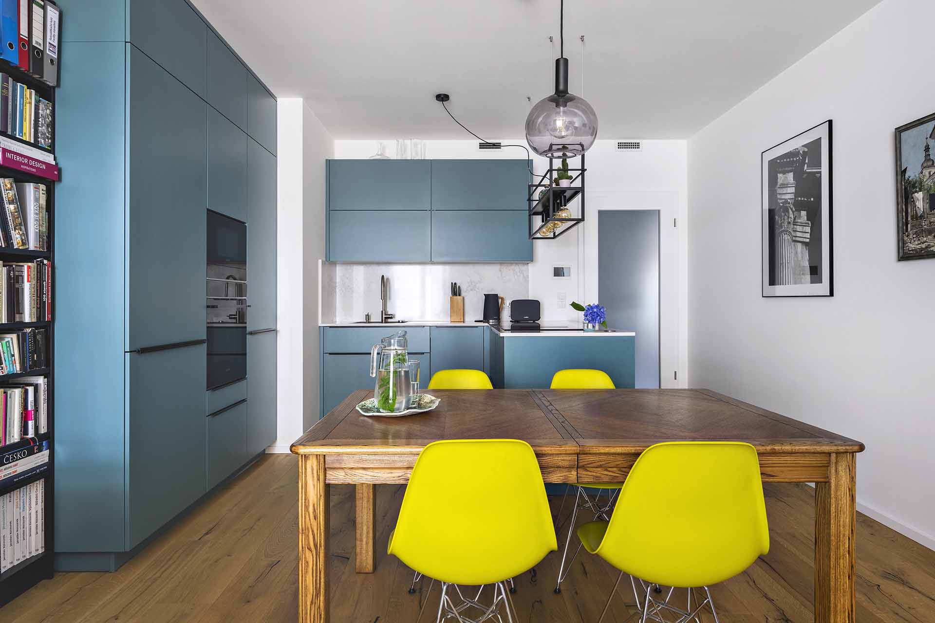 Moderní kuchyně na míru s ostrůvkem, petrolejovými skříňkami a designovým závěsným osvětlením.