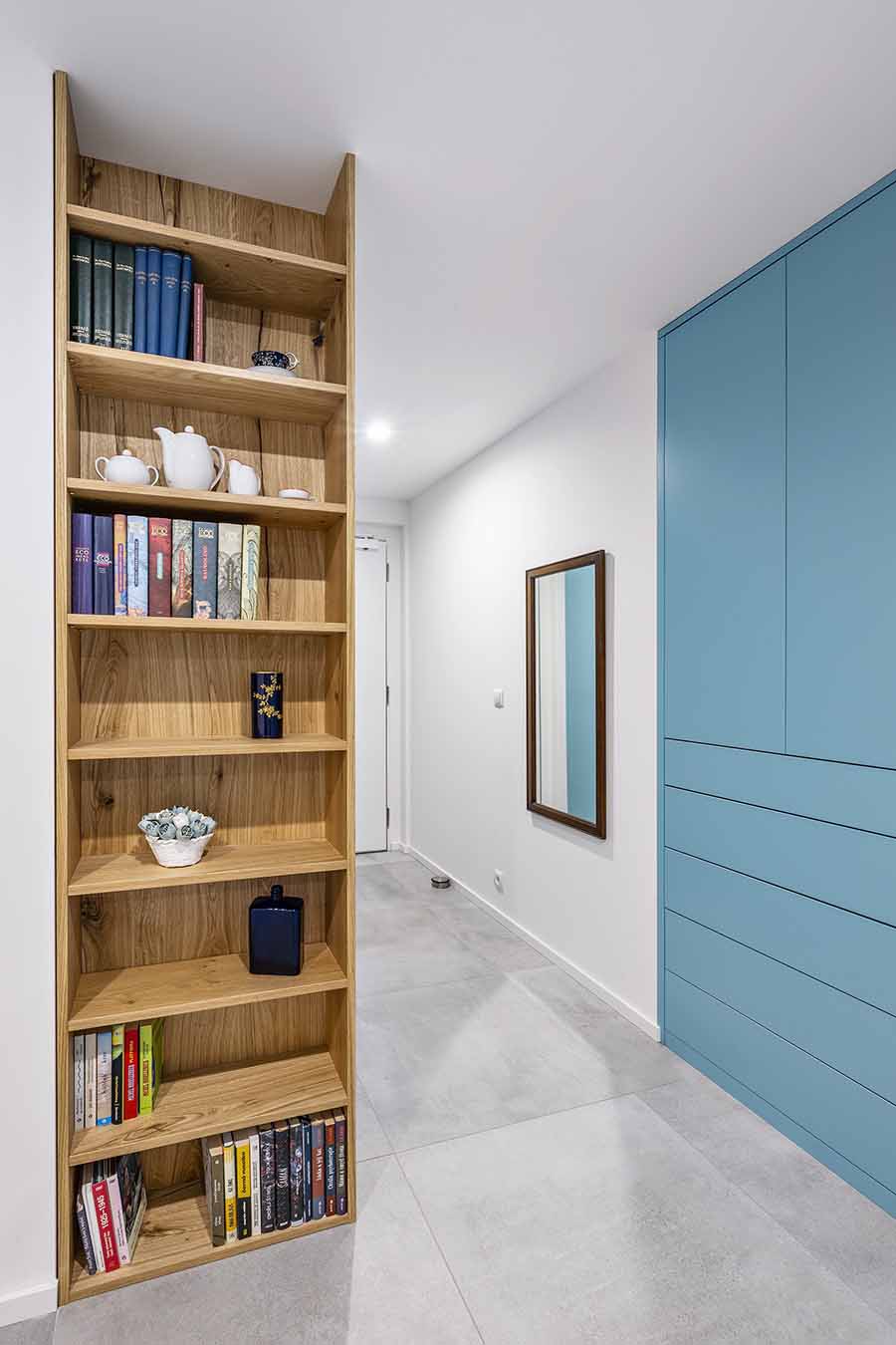 Předsíň s vestavěnými skříněmi a knihovnou ze světlého dřeva, doplněná o dekorace a knihy.